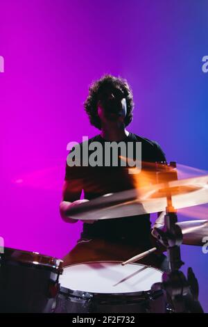 Silhouette of young man drummer playing isolated on blue-pink background in neon Stock Photo