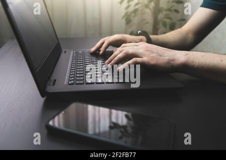 Male person use laptop at his home. Side view shot of man working and typing on keyboard at his home or office Stock Photo