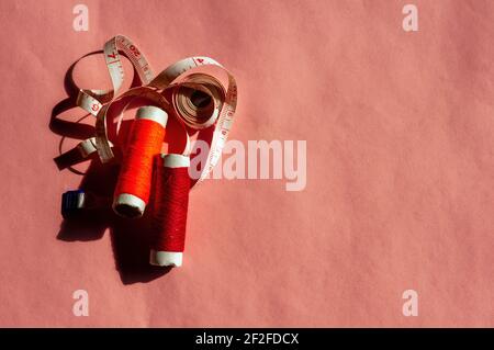 Colorful sewing threads and a tape measure on pink background Stock Photo