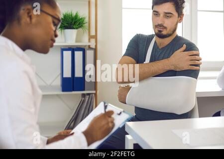 Doctor prescribing treatment to young patient with broken hand, wrist, elbow or arm Stock Photo