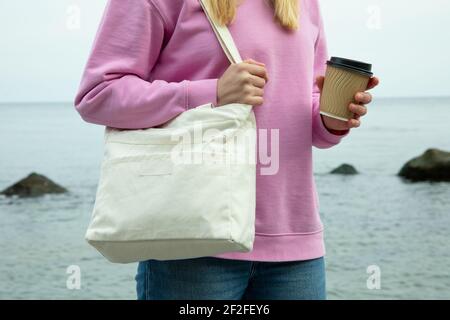 Young woman hold stylish eco bag and paper cup against sea Stock Photo
