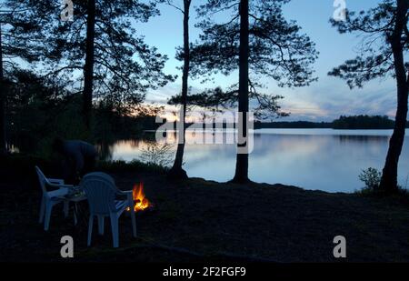 DACKESKOGEN, SWEDEN ON MAY 13, 2012. View of the Nordic night with Nordic light by a lake. Campfire and seats. Editorial use. Stock Photo