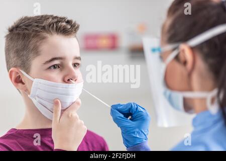 Young boy wearing face mask over mouth holds still as nurse takes a sample from his nose using swab. Stock Photo