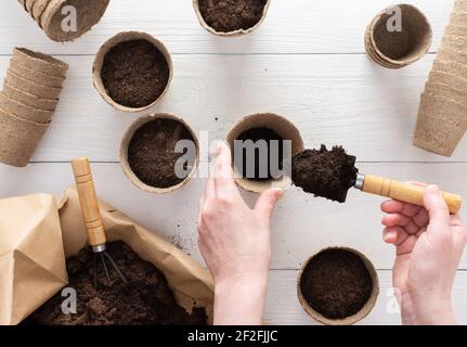 Eco friendly pots for seedlings and a bag with ground on a white wooden background, the gardener pours soil in the pots for planting seeds, top view Stock Photo