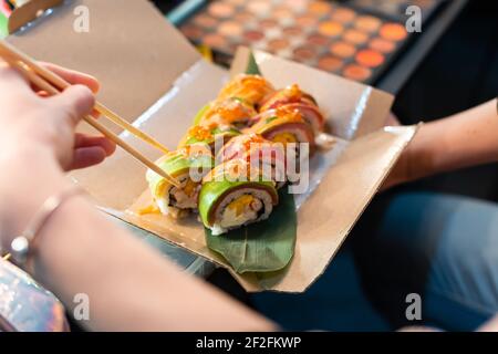 close up of chopsticks taking portion of sushi roll on the table restaurant. eating sushi roll using chopsticks Stock Photo