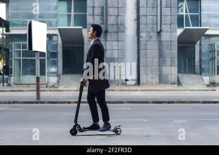 Asian businessman riding an electric scooter on the city streets to go to work in the morning. Daily commute that best reflect the working world of to Stock Photo