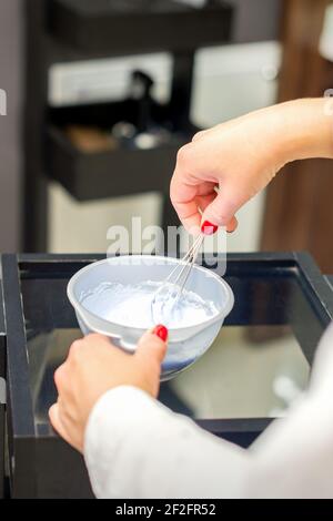 The hairstylist makes a white color dye mix for coloring hair at a salon close-up. Stock Photo