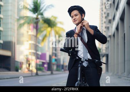 Asian businessman in suits are wearing safety helmets to cycle on city streets for their morning commute to work. Eco transportation. Stock Photo