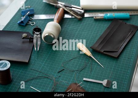 Mens hand working on the leather wallet in his workshop. Working process with a brown natural leather. Craftsman holding a crafting tools. Stock Photo