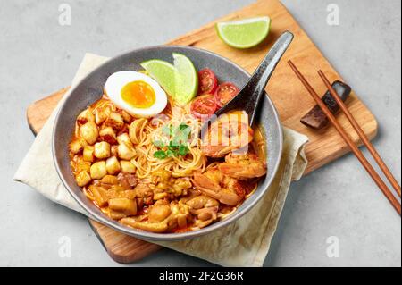 Laksa in gray bowl on concrete table top. Coconut noodle soup with chicken meat and prawns of peranakan cuisine. Asian food. Stock Photo