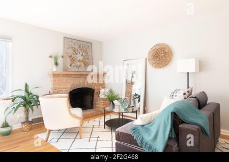 A bright, beautiful living room with furniture and an area rug on hardwood floors in front of a fireplace. Stock Photo