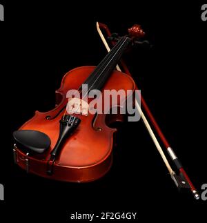 An old rustic child's violin with a bow isolated in black background Stock Photo