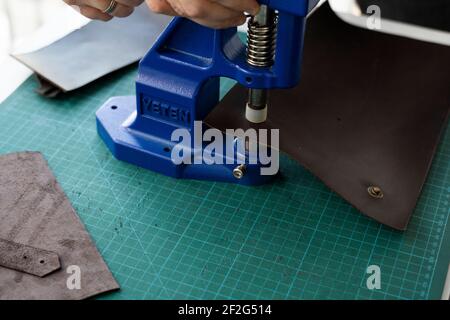 Artisan using hand press for setting snaps in leather for makes a wallet. Hand Pressure Snap Pressing Machine is using by craftsman in leather Stock Photo