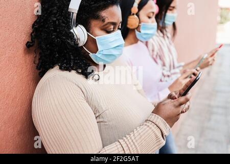 Young multiracial friends wearing protective masks while using mobile phone outdoors - Focus on right hand Stock Photo