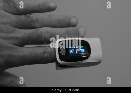 fingertip pulse oximeter equipment connected to the index finger of a young man measuring oxygen saturation in blood and heart rate. Stock Photo