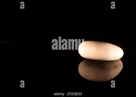 Closeup of a white marble pebble lying on a black reflective surface Stock Photo