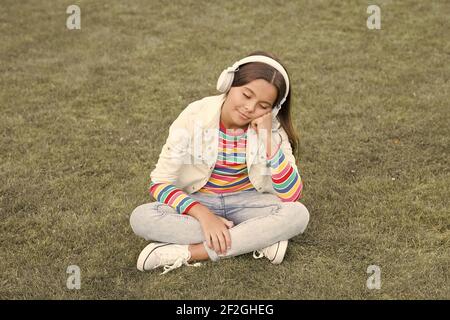 doze off. enjoy spring nature outdoor. child study audio book. new technology. Child listen music on green grass. Healthy lifestyle and relax. Yoga girl. small kid in headphones. summer playlist. Stock Photo