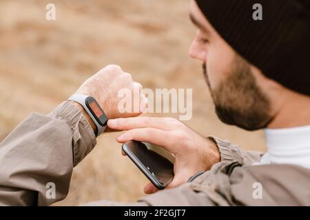 Focused handsome man using smartwatch and cellphone while working out in nature Stock Photo