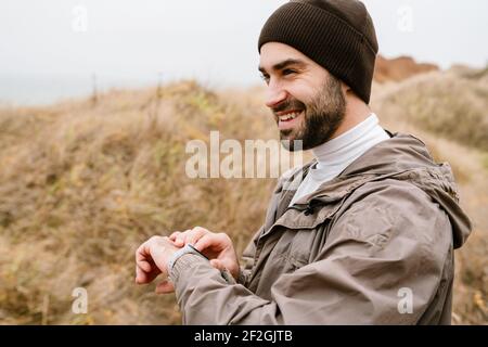 Happy handsome man smiling and using smartwatch while working out in nature Stock Photo