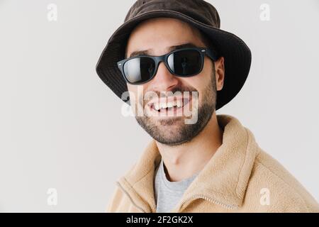 Portrait of a happy young man wearing beige jacket, cap and sunglasses on isolated white background, close up Stock Photo