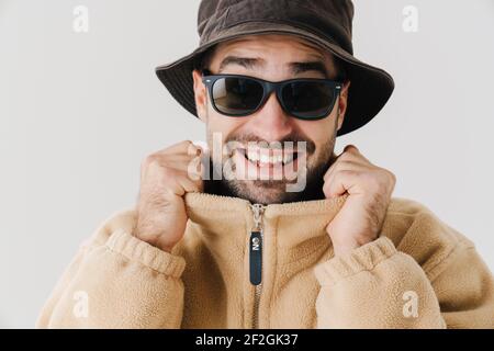 Portrait of a happy young man wearing beige jacket, cap and sunglasses on isolated white background, close up Stock Photo