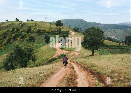 Man biking old motorcycle on gravel road down to green hill at countryside Stock Photo