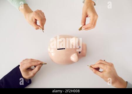 From above shot of people's hands putting money in pink piggy bank on white background Stock Photo