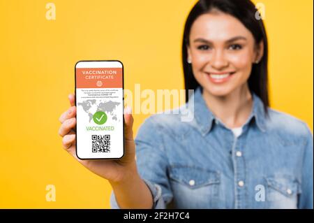 Defocused woman holds smartphone displaying valid digital vaccination certificate and QR code on isolated background. Digital vaccination passport for COVID19 for for all people who travel Stock Photo
