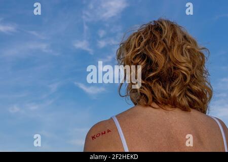 Blonde woman turned away with the word "Kona" which in Icelandic means woman on one shoulder, against a beautiful blue sky with white clouds Stock Photo