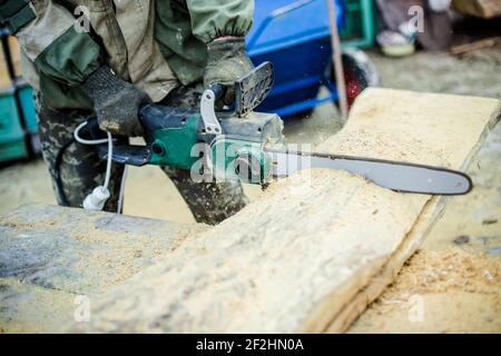 Saws in hand fitter. The man saws a thick piece of wood. From the saw chips fly. Stock Photo