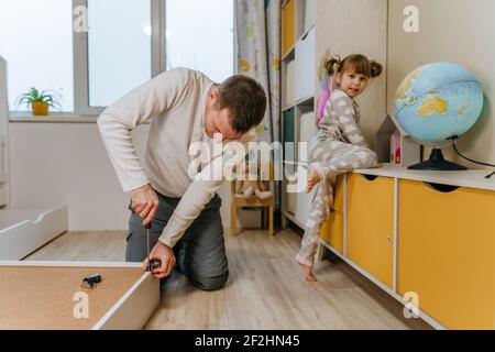 Little 4-years girl helps her father assemble or fixing the drawer of bed in the kids bedroom. Stock Photo