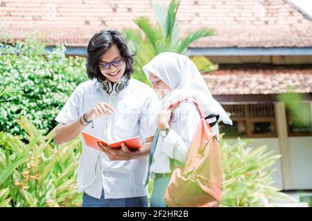 High school boy wearing glasses and headphone holding book with female veiled student Stock Photo