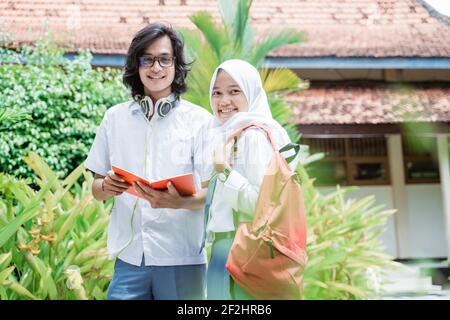 High school boy wearing glasses and headphone holding book with veiled female students standing smiling at the camera Stock Photo