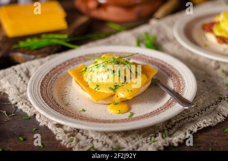 Organcic eggs benedict with bacon, cheddar cheese and herbs and hollandaise sauce Stock Photo