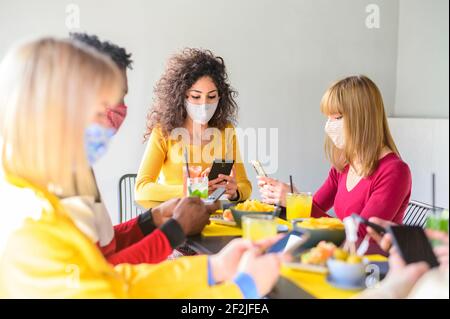 Group of friends using mobile smart phones at coffee bar - Teenagers texting mobile phone messages sitting at restaurant - New normal concept about fr Stock Photo