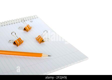 Notebook, pencil and binder clips on white background. Blank spiral striped notepad with orange crayon and binder clips on it. Stock Photo