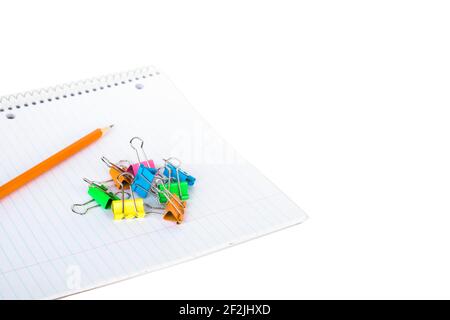 Stationary on white background with empty space. Notebook, pencil and binder clip. Blank spiral striped notepad with orange crayon and binder clips on Stock Photo