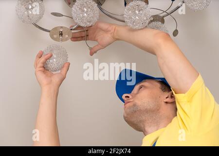 Electrician screws the ceiling light from the chandelier on the stretch ceiling close-up Stock Photo