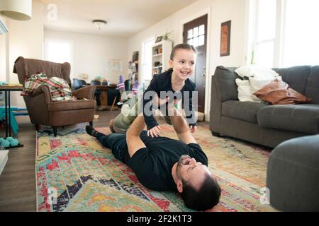 Father doing airplane with a little girl on the floor. Stock Photo