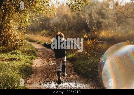 Rear view of boy jumping over muddy puddle on canal side path Stock Photo