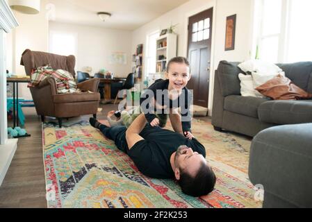 Father doing airplane with little girl on living room floor. Stock Photo
