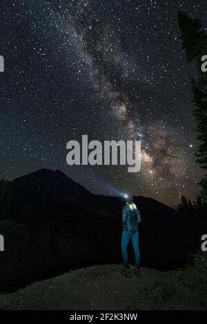 Woman with head lamp standing by Copper Lake against star field at night Stock Photo