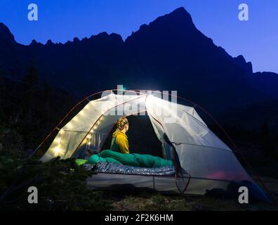 Woman sitting in illuminated tent on mountain at night Stock Photo