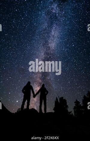 Silhouette couple holding hands while standing against beautiful star field at night Stock Photo