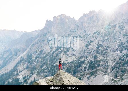 Rear view of woman standing on rock against mountain while hiking during vacation Stock Photo