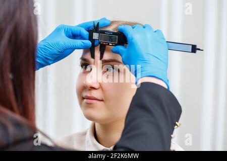 A woman permanent makeup artist draws a sketch of the eyebrows on the face of her client. Stock Photo