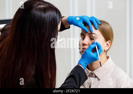 A woman permanent makeup artist draws a sketch of the eyebrows on the face of her client. Stock Photo