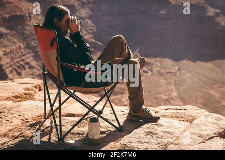 Side view of man looking through binoculars while sitting on chair at Canyonlands National Park Stock Photo