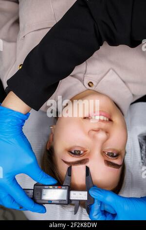 Woman with permanent makeup tattoo on her eyebrows. Close-up beautician makes a sketch of the eyebrows. Professional make-up and cosmetic skin care. Stock Photo