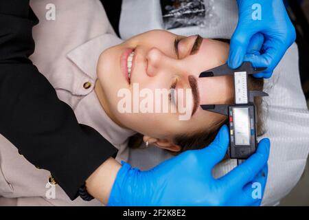 Woman with permanent makeup tattoo on her eyebrows. Close-up beautician makes a sketch of the eyebrows. Professional make-up and cosmetic skin care. Stock Photo